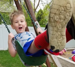 A boy swinging on a swingset with his feet in the air, close to the camera